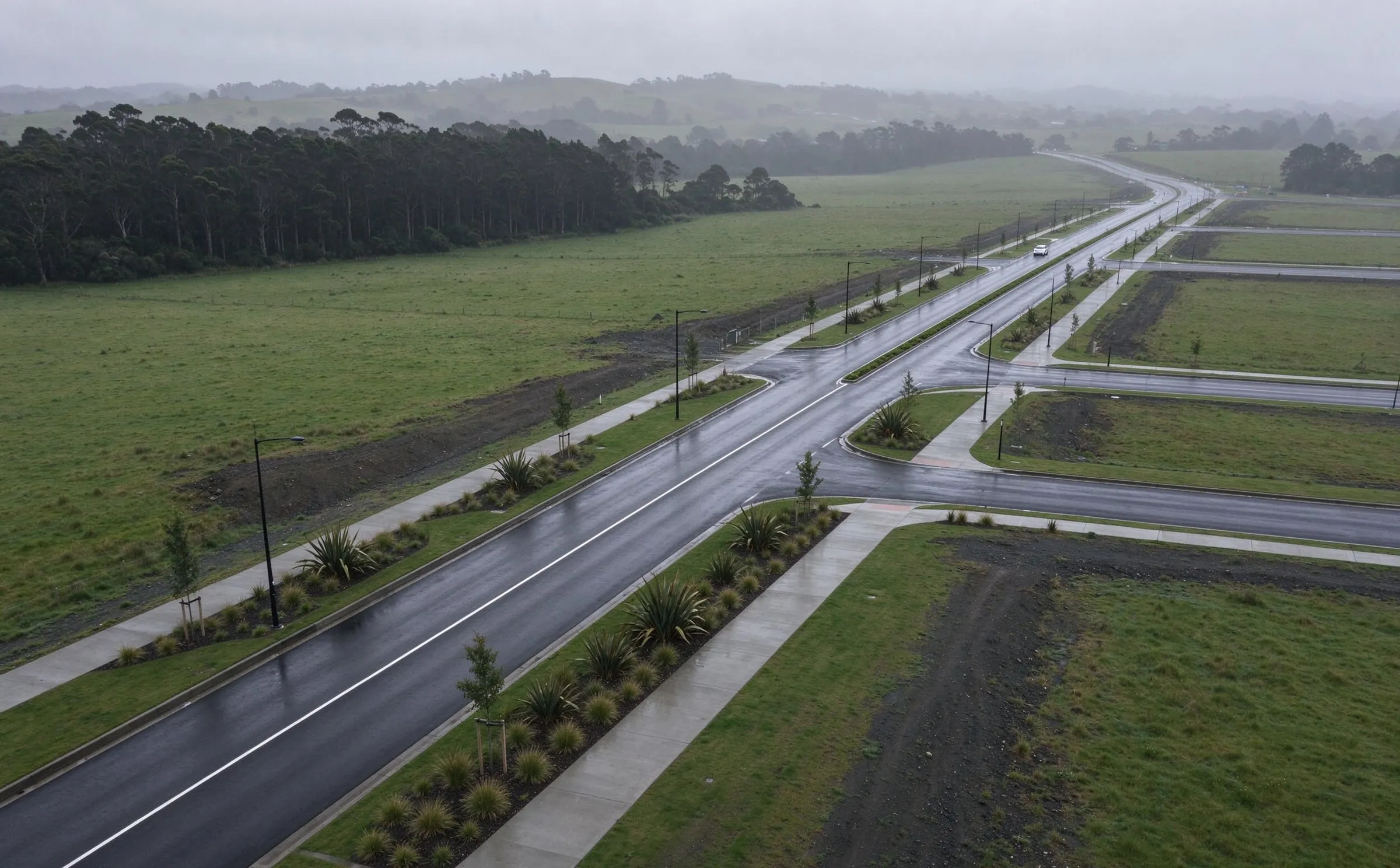 Aerial view of a new arterial road after rain, with planted berms, footpaths and side roads